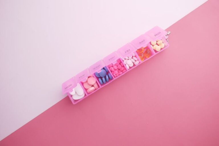 Pilulier électronique - A pink pill organizer with colorful tablets arranged for each day of the week on a vibrant pink background.